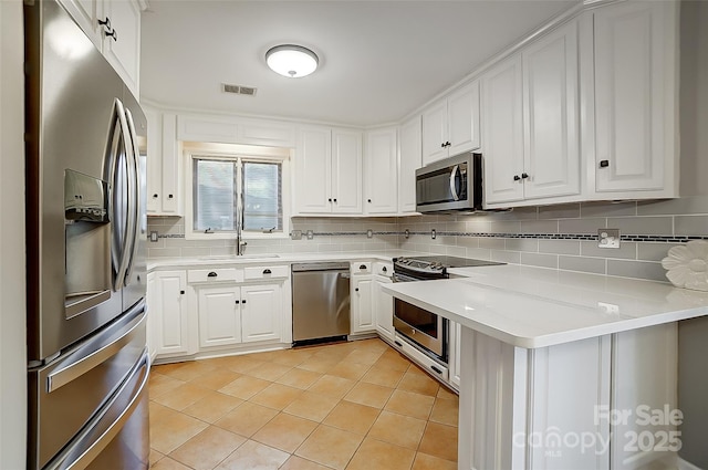 kitchen featuring kitchen peninsula, stainless steel appliances, light tile patterned floors, white cabinetry, and sink