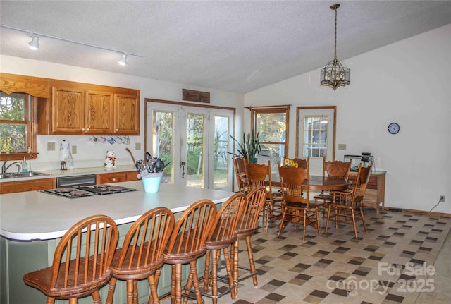 kitchen with vaulted ceiling, pendant lighting, sink, an inviting chandelier, and a textured ceiling