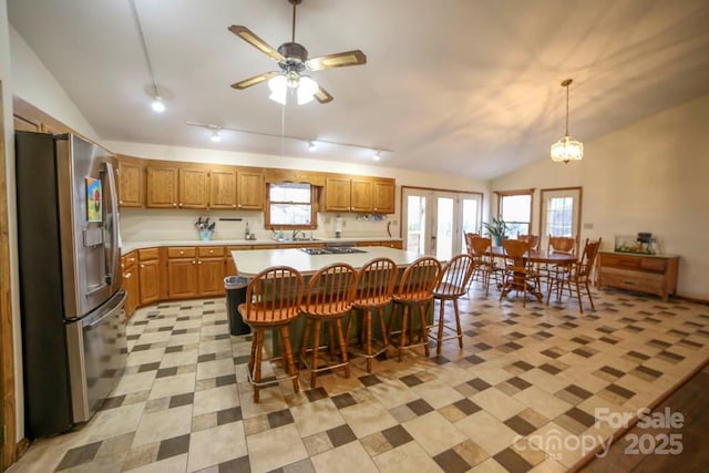 kitchen with vaulted ceiling, a kitchen island, a kitchen bar, stainless steel fridge with ice dispenser, and ceiling fan with notable chandelier