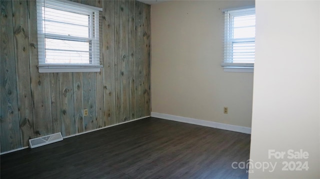 spare room with dark hardwood / wood-style flooring, a wealth of natural light, and wood walls