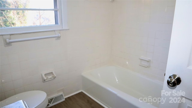 bathroom with hardwood / wood-style flooring, toilet, and a tub to relax in