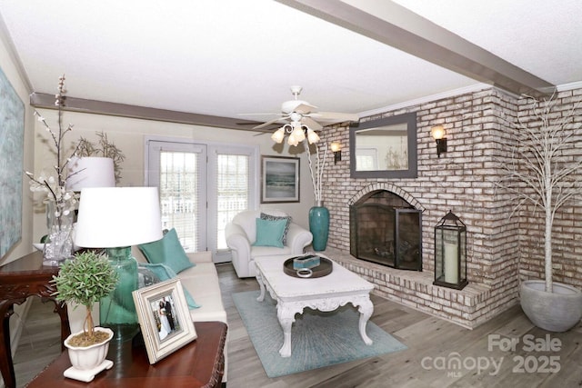 living room featuring hardwood / wood-style flooring, ceiling fan, a brick fireplace, and beamed ceiling