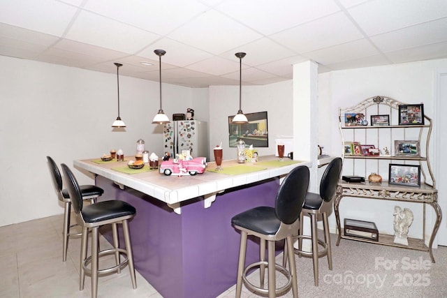 kitchen with refrigerator, a kitchen breakfast bar, hanging light fixtures, kitchen peninsula, and a drop ceiling