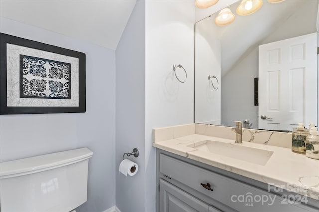 bathroom featuring toilet, vanity, and vaulted ceiling