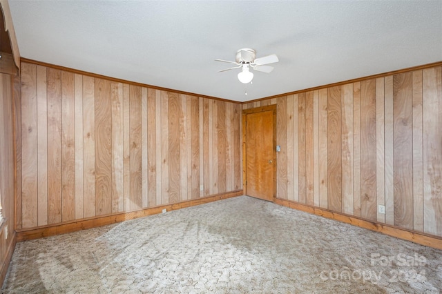 unfurnished room with carpet, a textured ceiling, ceiling fan, and wooden walls