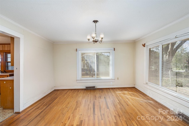 unfurnished dining area with a textured ceiling, an inviting chandelier, light hardwood / wood-style flooring, and ornamental molding