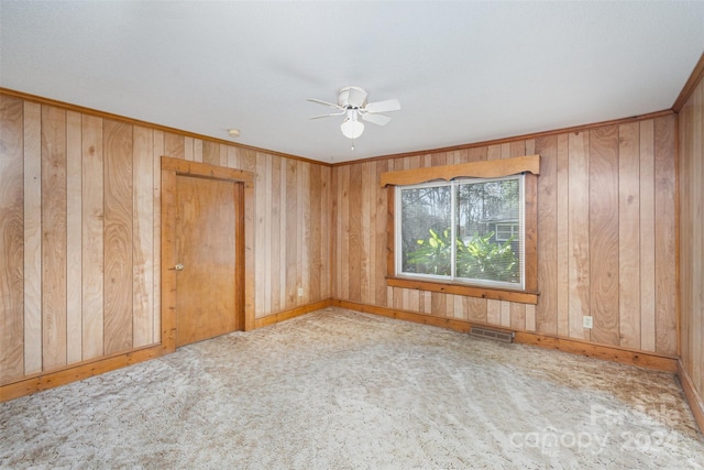 carpeted spare room featuring ceiling fan, wood walls, and ornamental molding