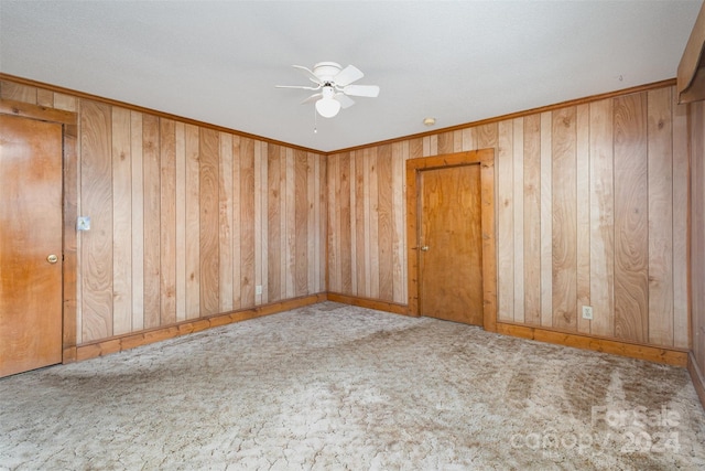 empty room featuring carpet, ceiling fan, crown molding, and wood walls