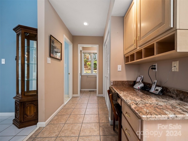 kitchen with light brown cabinets, light tile patterned floors, built in desk, and light stone countertops