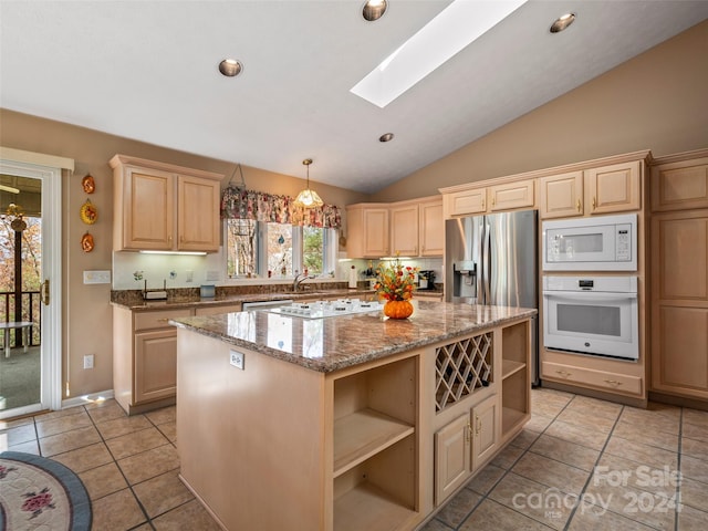 kitchen featuring light stone counters, a center island, light tile patterned floors, vaulted ceiling with skylight, and white appliances