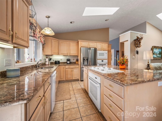 kitchen with sink, vaulted ceiling with skylight, light brown cabinetry, light tile patterned floors, and white appliances