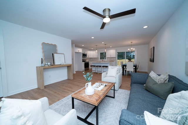 living room with sink, light wood-type flooring, and ceiling fan with notable chandelier