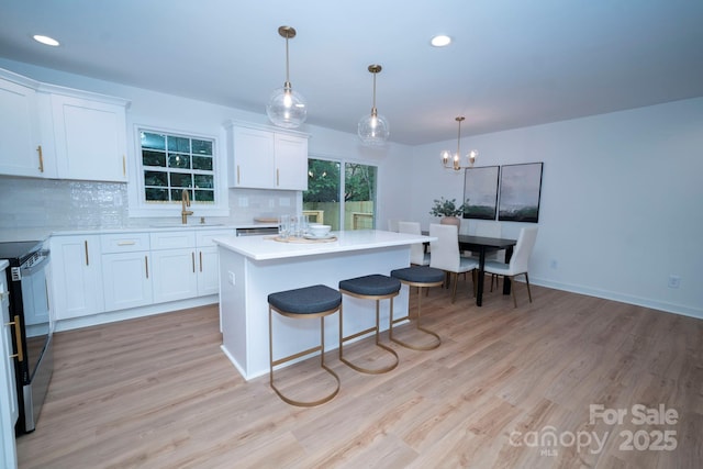 kitchen featuring stainless steel electric stove, white cabinets, light hardwood / wood-style flooring, backsplash, and hanging light fixtures