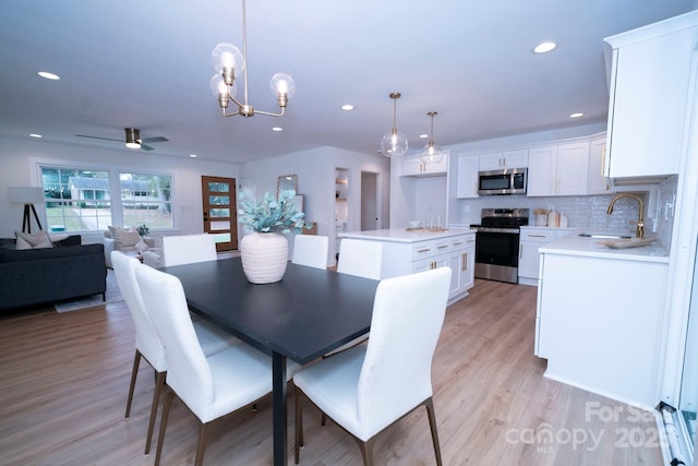 dining room with sink, light hardwood / wood-style floors, and ceiling fan with notable chandelier