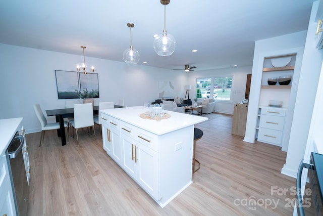 kitchen featuring light wood-type flooring, a center island, pendant lighting, white cabinetry, and ceiling fan with notable chandelier