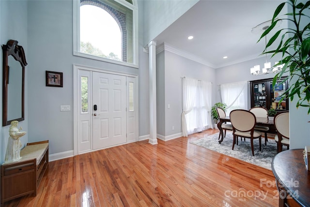 entrance foyer with decorative columns, crown molding, a chandelier, a high ceiling, and light hardwood / wood-style floors