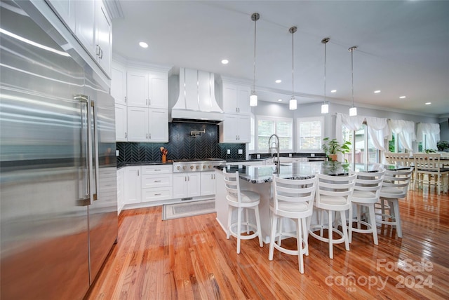 kitchen featuring pendant lighting, light wood-type flooring, custom range hood, white cabinetry, and stainless steel appliances