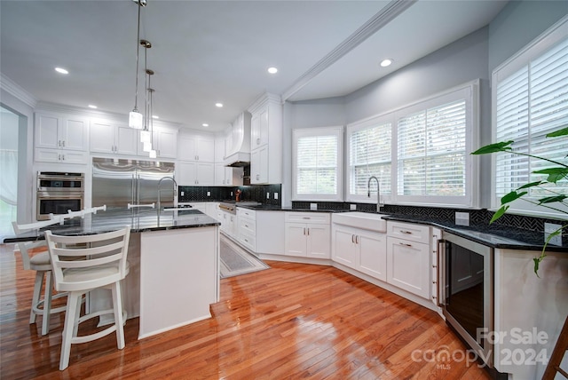 kitchen featuring white cabinets, beverage cooler, a kitchen island with sink, and appliances with stainless steel finishes