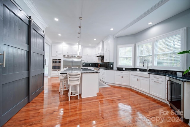 kitchen with a barn door, wine cooler, light hardwood / wood-style flooring, an island with sink, and appliances with stainless steel finishes