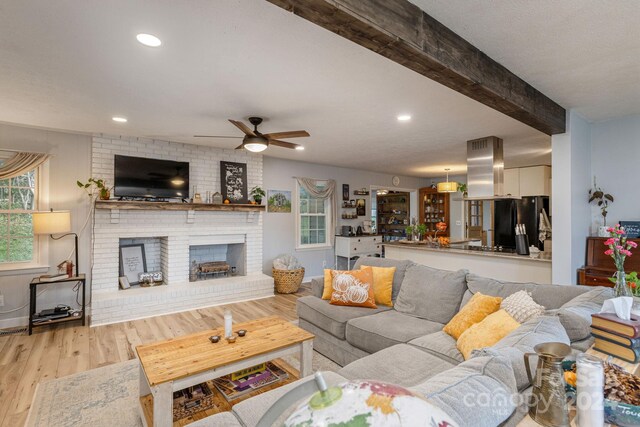 living room featuring a fireplace, ceiling fan, beam ceiling, and light wood-type flooring