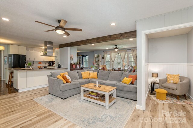 living room featuring beamed ceiling, ceiling fan, a textured ceiling, and light wood-type flooring