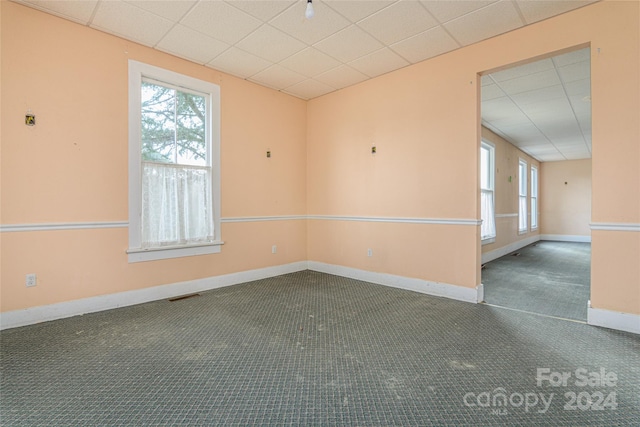 empty room featuring dark colored carpet, plenty of natural light, and a drop ceiling