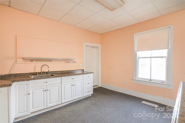 kitchen with white cabinetry, sink, a drop ceiling, and dark carpet