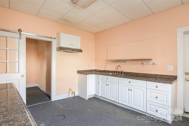 kitchen with a barn door, sink, white cabinets, and dark colored carpet