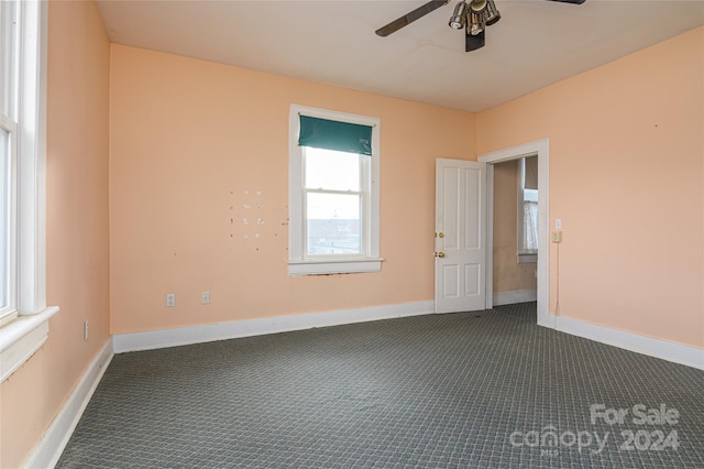 empty room featuring ceiling fan and dark colored carpet