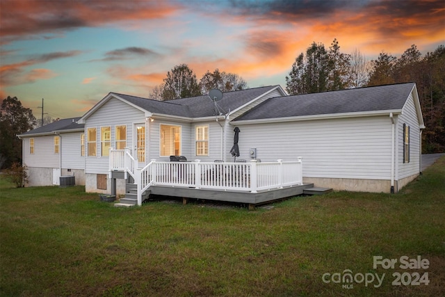 back house at dusk featuring central AC unit, a wooden deck, and a lawn