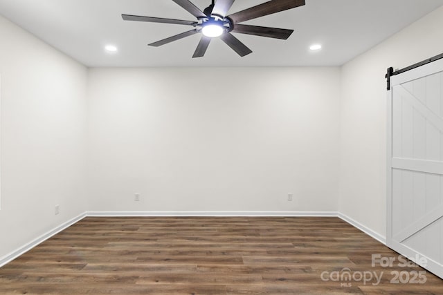 empty room featuring dark hardwood / wood-style flooring, a barn door, and ceiling fan