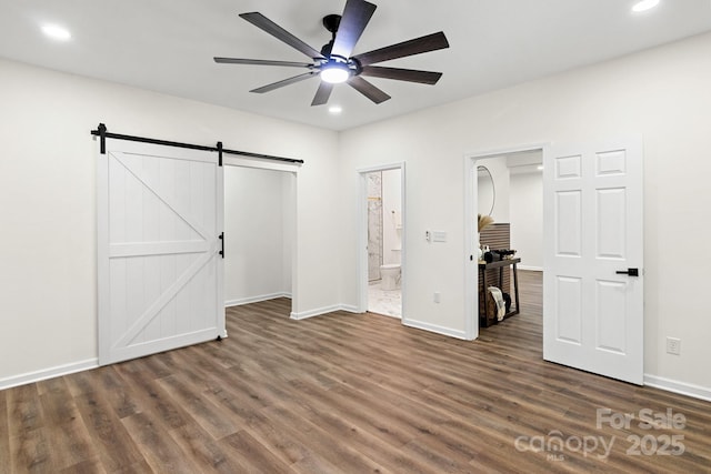 unfurnished bedroom with a barn door, dark hardwood / wood-style floors, ensuite bath, and ceiling fan