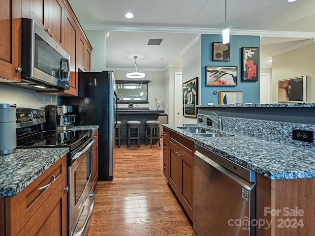 kitchen with crown molding, appliances with stainless steel finishes, pendant lighting, sink, and light hardwood / wood-style floors