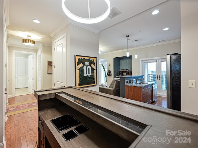 kitchen featuring ornamental molding, light wood-type flooring, appliances with stainless steel finishes, sink, and a kitchen island with sink