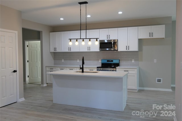 kitchen featuring stove, a center island with sink, white cabinets, hanging light fixtures, and light hardwood / wood-style flooring