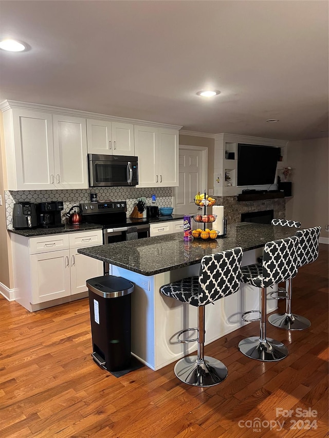 kitchen with stainless steel appliances, backsplash, light hardwood / wood-style floors, white cabinets, and a breakfast bar