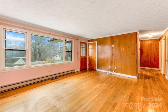 empty room with ornamental molding, a textured ceiling, wooden walls, a baseboard heating unit, and light hardwood / wood-style flooring