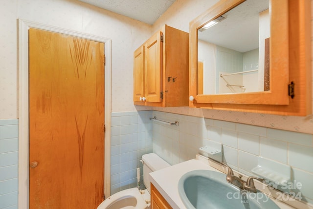 bathroom with vanity, a textured ceiling, toilet, and tile walls