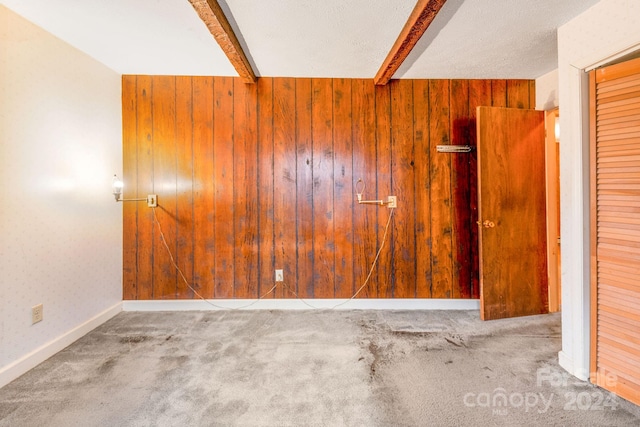 carpeted empty room with beamed ceiling and wooden walls