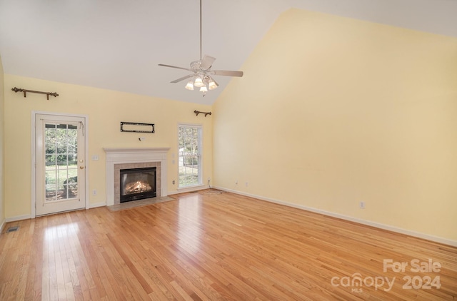 unfurnished living room with high vaulted ceiling, light wood-type flooring, a wealth of natural light, and a tile fireplace