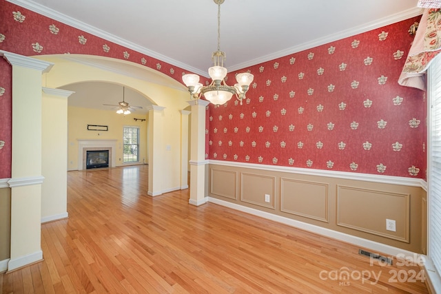 spare room featuring ceiling fan with notable chandelier, wood-type flooring, crown molding, and decorative columns