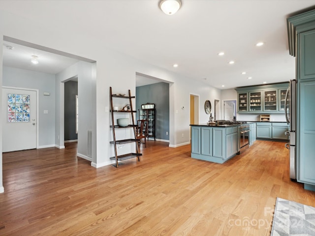 kitchen with light wood-type flooring, stainless steel refrigerator, and an island with sink