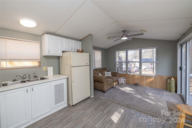 kitchen featuring white fridge, wood walls, sink, light hardwood / wood-style floors, and white cabinets