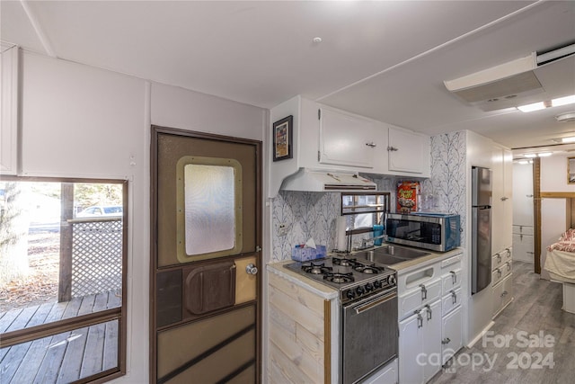 kitchen featuring white cabinetry, appliances with stainless steel finishes, light hardwood / wood-style flooring, premium range hood, and decorative backsplash