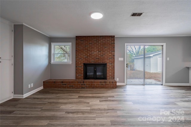 unfurnished living room featuring a brick fireplace, a textured ceiling, ornamental molding, and hardwood / wood-style flooring