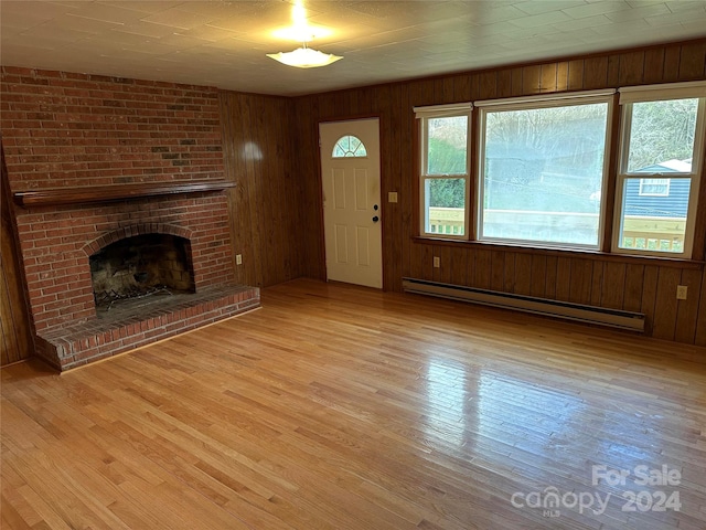 unfurnished living room featuring wood walls, a fireplace, light wood-type flooring, and a baseboard heating unit