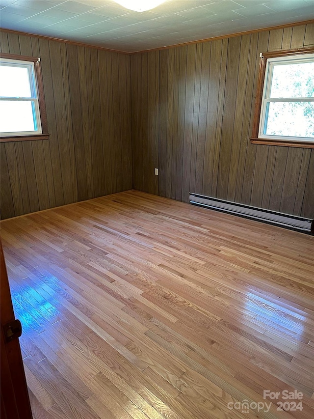 unfurnished room featuring a baseboard radiator, light wood-type flooring, a wealth of natural light, and wood walls