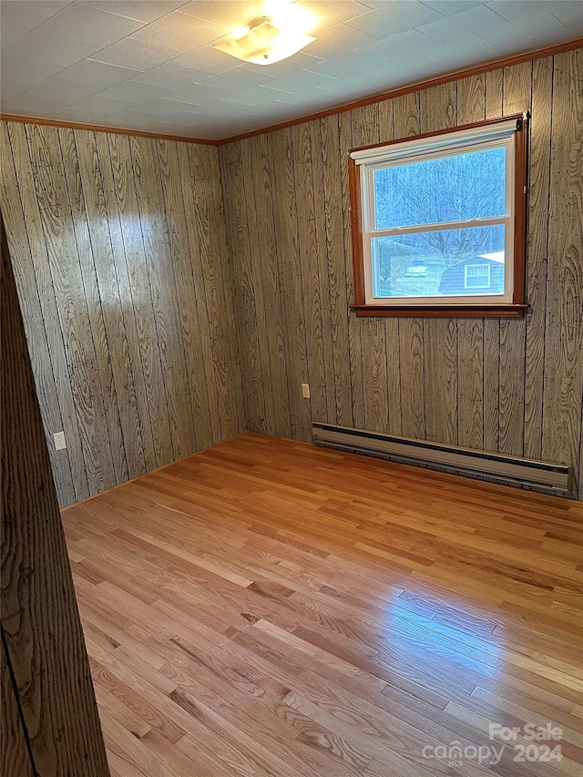 spare room with light hardwood / wood-style flooring, wood walls, and a baseboard radiator