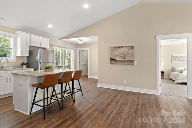 kitchen with a breakfast bar, vaulted ceiling, stainless steel fridge, a kitchen island, and white cabinetry