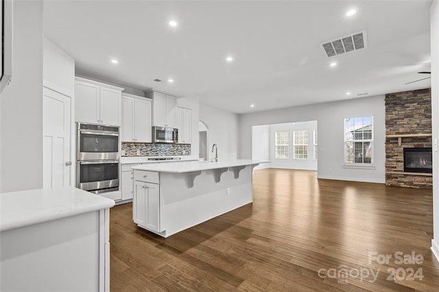 kitchen with white cabinets, appliances with stainless steel finishes, a kitchen island with sink, and dark wood-type flooring